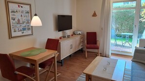 Un espace de vie compact comprenant une table à manger en bois, des chaises rouges, un téléviseur et un meuble.