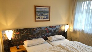 Une chambre d’hôtel avec deux lits, une table de chevet avec une horloge, un tableau encadré au mur et une fenêtre avec des rideaux.