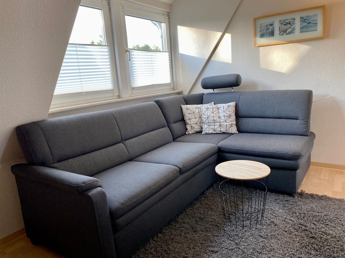 En moderne stue med en grå modulsofa, et lille rundt træsofabord og en grå, lurvet måtte.