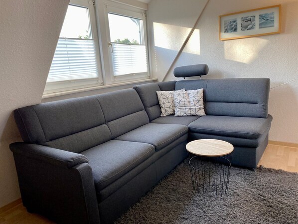 Una sala moderna con un sofá seccional gris, una mesita redonda de madera y una alfombra mullida gris.