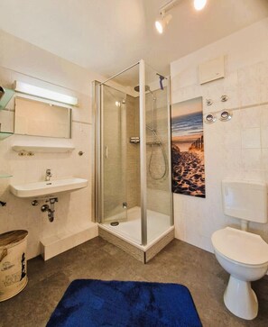 Une salle de bain avec une douche à parois de verre, un lavabo blanc, des toilettes et une décoration murale sur le thème de la plage.