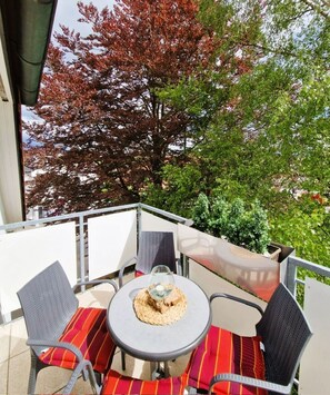 Un balcon avec une table ronde, deux chaises et un verre d’eau.