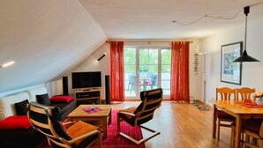 Un espacio habitable moderno tipo loft con comedor, sofá, televisor y un amplio ventanal con cortinas.