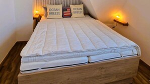 Ett sovrum med en sängram i trä, två sänglampor och ett sluttande tak.
