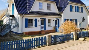 Ett tvåvåningshus med ett blått tak, vita väggar och blåa fönsterluckor. Framför huset finns ett blått staket.