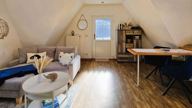 En mysig lägenhet i ett loft med högt i tak, trägolv, en soffa, ett matbord och ett litet köksutrymme.