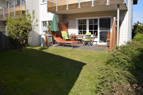 Eine Terrasse mit Tisch, Stühlen und einem grünen Sonnenschirm, sowie ein Holzdeck.