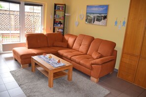 Ein Wohnzimmer mit einem Ecksofa, einem Holztisch, einem Bücherregal und einem Bild an der Wand.