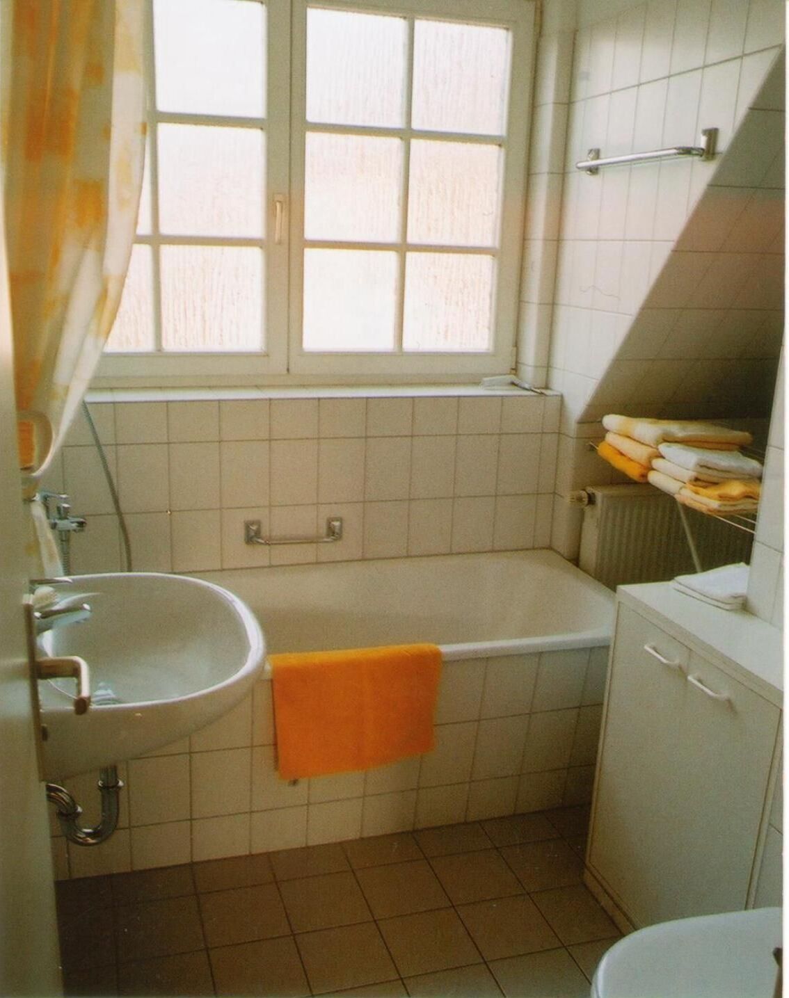 A small bathroom with a window, a sink, a bathtub, and a towel rack.