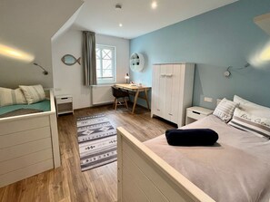 Ein Schlafzimmer mit Bett, Schreibtisch, Kleiderschrank, Heizkörper und einem Fenster mit Vorhängen.
