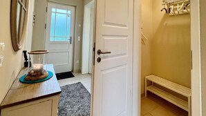 A hallway with a white door, a small bench, a rug, and a coat rack with hangers.