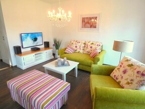 A living room with a sofa, a coffee table, a TV, and a chandelier.