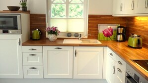 Una cocina moderna con armarios blancos, encimera de madera, horno empotrado y ventana con cruces.