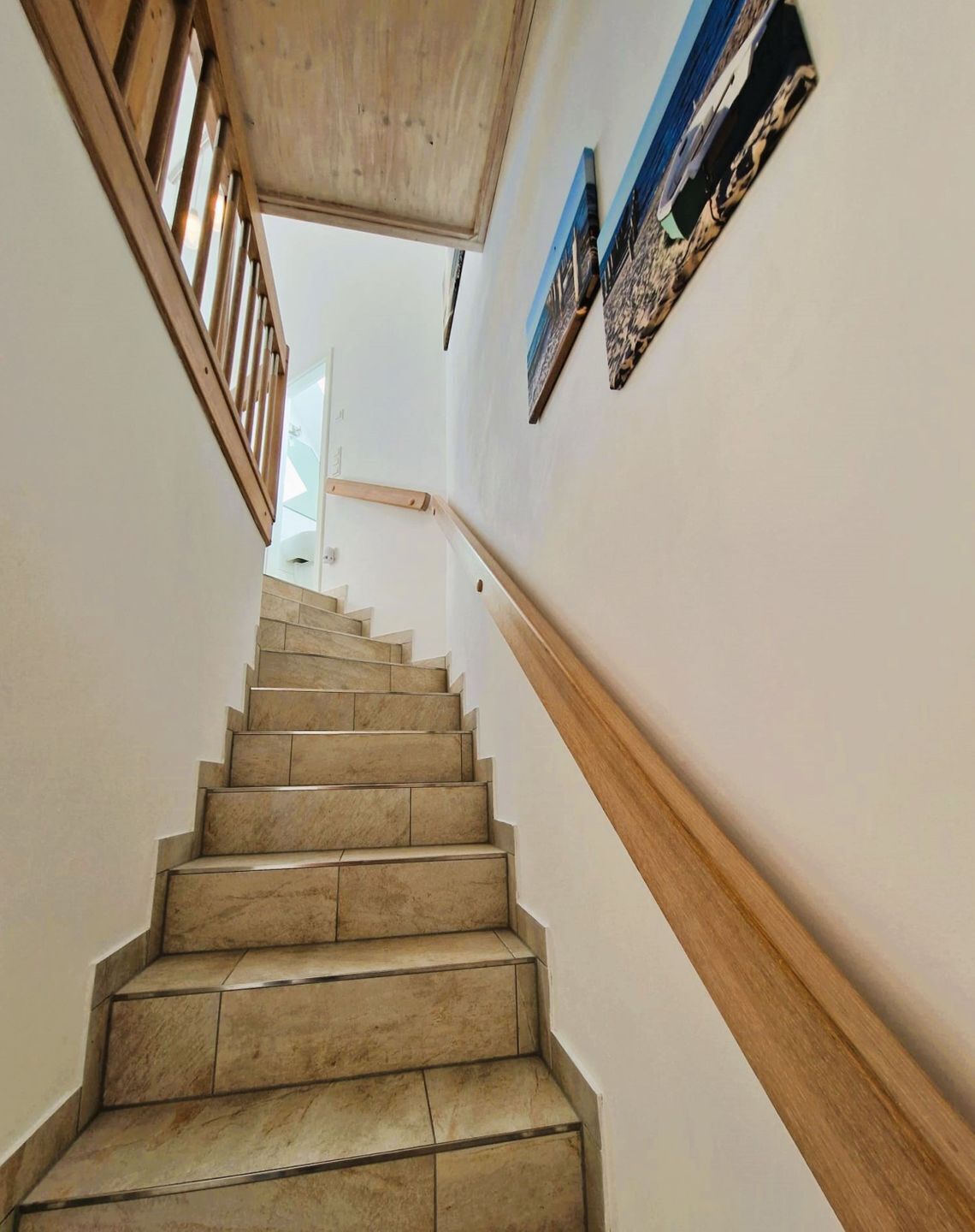 A staircase with wooden handrails and beige tiles, leading to a room with a view of the sky.
