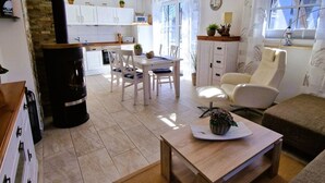 Un salon moderne comprenant un canapé, une table basse et un coin repas avec une table et des chaises. Au fond, on aperçoit une cuisine avec des meubles blancs et un fourneau noir.