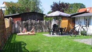 Een achtertuin met een houten hek, een patio tafel en stoelen, een fiets en een tuinhuis.