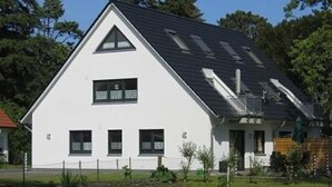 A white building with a triangular roof, a small porch, and a fenced yard. - Schulstrasse 10a (App) - cozy 1-room apartment (Zingst)