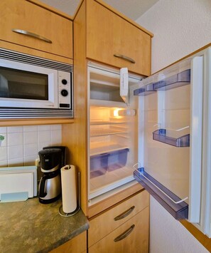A compact kitchen with a microwave, coffee maker, and a refrigerator with clear plastic bins.