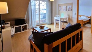 A cozy room with a wooden sofa, a small table, a TV, and a balcony with a view. - Fritz-Reuter-Str. 2 Whg. 7 "Sonnenuhr" - A lovingly furnished apartment (Zingst)