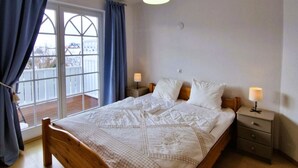 A bedroom with a wooden bed, a nightstand, a lamp, and a view of a balcony. - Fritz-Reuter-Str. 2 Whg. 7 "Sonnenuhr" - A lovingly furnished apartment (Zingst)