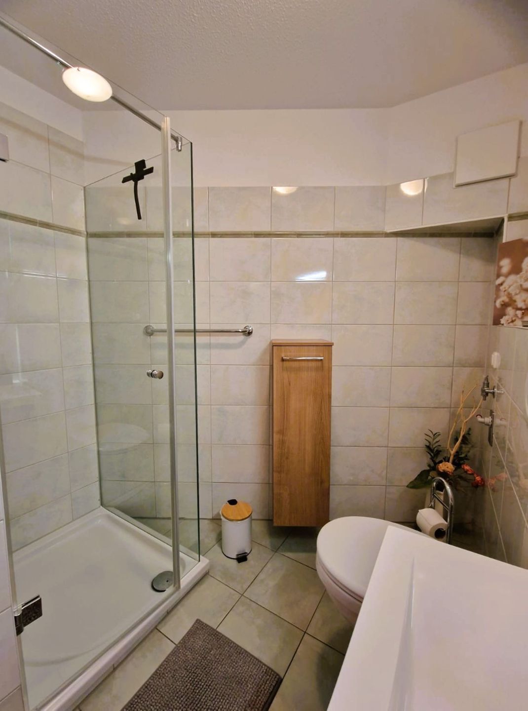 A bathroom with a glass shower enclosure, a wooden cabinet, a toilet, and a sink.