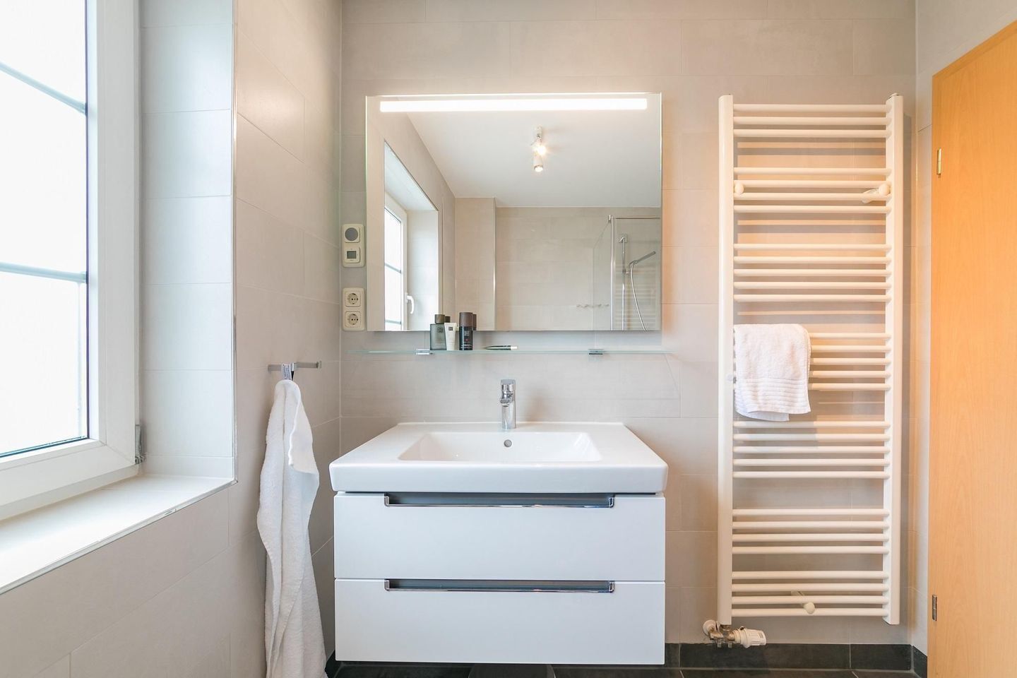 Casa de banho moderna com lavatório branco, espelho e porta-toalhas.