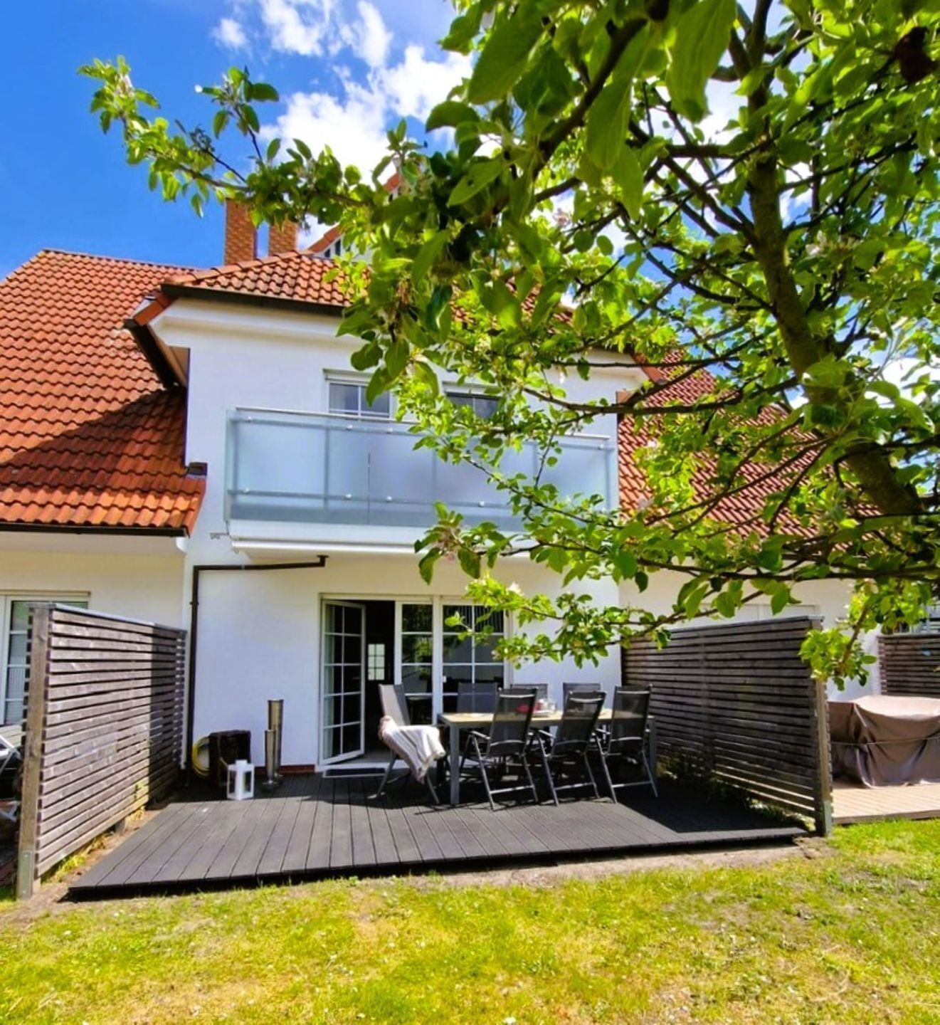 A two-story house with a balcony, a patio with outdoor furniture, and a wooden deck.