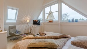 A bedroom with a bed, a chair, a desk, a TV, and a sailboat model. - Haus Kranichsruh Whg.2.3 "strandgut" (Zingst)
