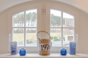 Una habitación con un ventanal grande de arco, una cesta de mimbre con el número 197, y pilas de recipientes con un diseño azul y blanco.