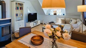 A modern living room with a wooden dining table, a sofa, a TV, and a bookshelf. - Haus Kranichsruh Whg.2.3 "strandgut" (Zingst)