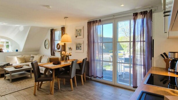 A modern kitchen with a wooden countertop and a built-in sink, a dining area with a wooden table and chairs, and a large sliding glass door leading to an outdoor patio. - Haus Kranichsruh Whg.2.3 "strandgut" (Zingst)