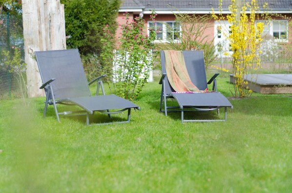 Dos sillones de exterior en un área con césped y una casa al fondo.