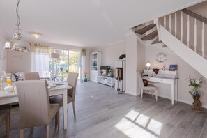 A spacious living area with a dining table, chairs, a kitchen area, a staircase, and a TV.