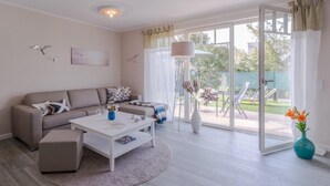 A modern living room with a sofa, coffee table, and a view of a garden through large sliding glass doors. - Birkmaase 1a "Abendklang" - comfortable semi-detached house "Abendklang" is quiet (Zingst)