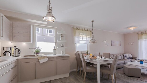 A modern kitchen with a dining area, featuring a central island, pendant lighting, and a view of the living room with a sofa and coffee table. - Birkmaase 1a "Abendklang" - comfortable semi-detached house "Abendklang" is quiet (Zingst)