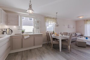 Una cocina moderna con comedor, que cuenta con una isla central, iluminación colgante y vistas al salón con un sofá y una mesa de centro.