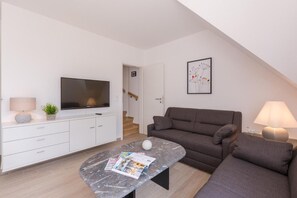 Un salon moderne avec un canapé gris, un téléviseur à écran plat, une table basse en marbre et un escalier menant à une porte.