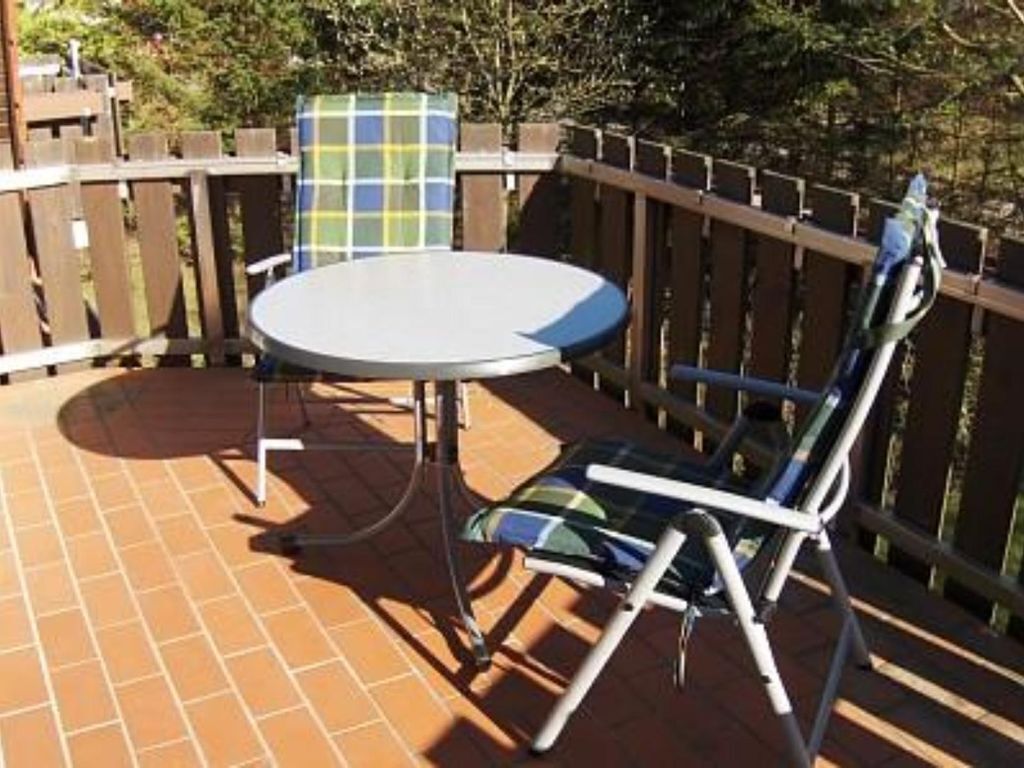 Een terras met een ronde tafel en twee stoelen, een houten schutting en een betegelde vloer.