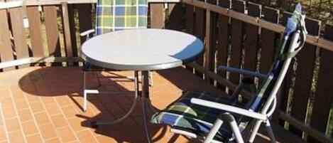 Een terras met een ronde tafel en twee stoelen, een houten schutting en een betegelde vloer.