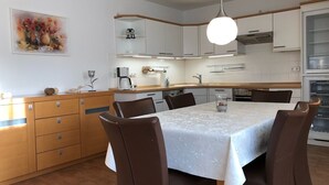 A modern kitchen with white cabinets, a dining table with chairs, a coffee machine, and a hanging light fixture. - Martha-Müller-Grählert-Weg 8 Whg. 7 - Spacious, modernly furnished (Zingst)