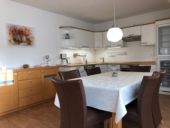 A modern kitchen with white cabinets, a dining table with chairs, a coffee machine, and a hanging light fixture. - Martha-Müller-Grählert-Weg 8 Whg. 7 - Spacious, modernly furnished (Zingst)