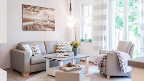 A modern living room with a grey sofa, a coffee table, and a chair. There is a painting on the wall and a window with curtains.
