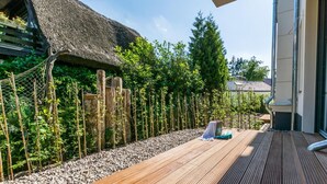 A wooden deck with a thatched-roof structure, a bamboo fence, and a garden area with various plants.