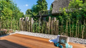 A wooden deck with a thatched-roof structure, surrounded by bamboo plants and a wooden fence.