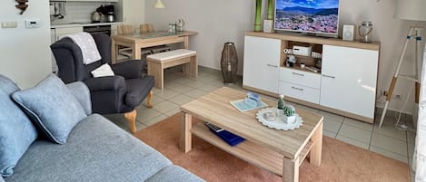 Uma sala de estar moderna com um sofá cinzento, uma mesa de centro de madeira e uma TV sobre um móvel branco.