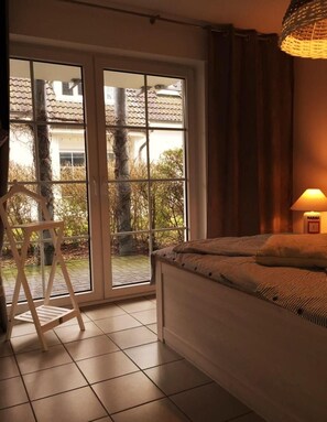 Un dormitorio con cama, una silla, una lámpara y vistas a través de un ventanal corredero.