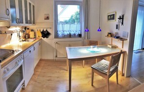 Uma cozinha compacta com mesa de jantar, armários de madeira, janela com vista e luminária pendente azul.