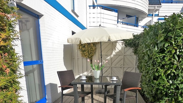 Une terrasse avec une table et des chaises, une plante en pot et un grand parasol.