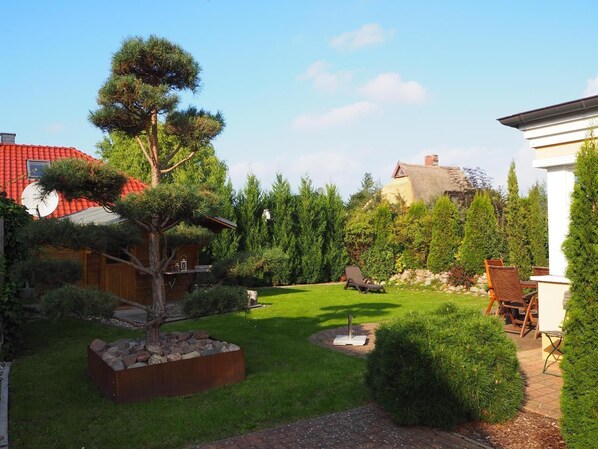 Een verzorgde tuin met gazon, een grote boom en een houten constructie.