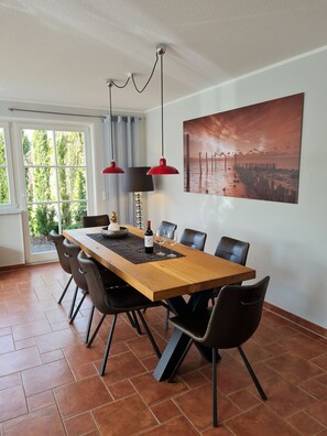 Un comedor con una mesa de madera, sillas negras, una lámpara colgante roja, una botella de vino y un cuadro en la pared.